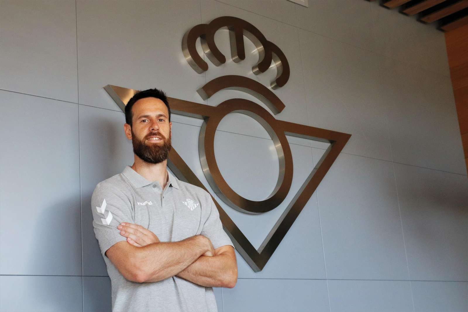 Pablo Almazán posando delante del escudo del Betis tras firmar su renovación con la entidad.