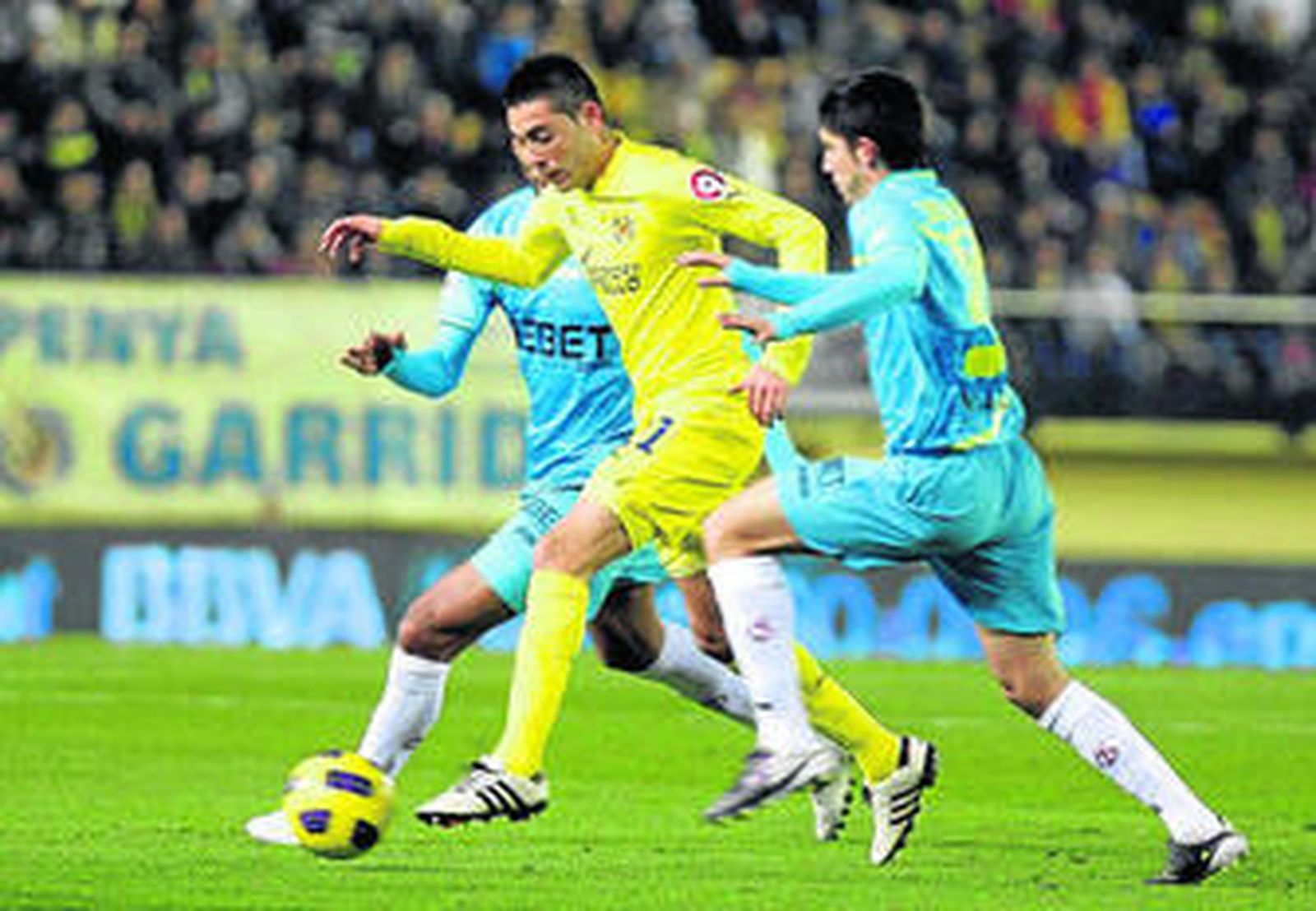 Cani, jugador del Villarreal, conduce el esférico perseguido por dos jugadores del Sevilla.