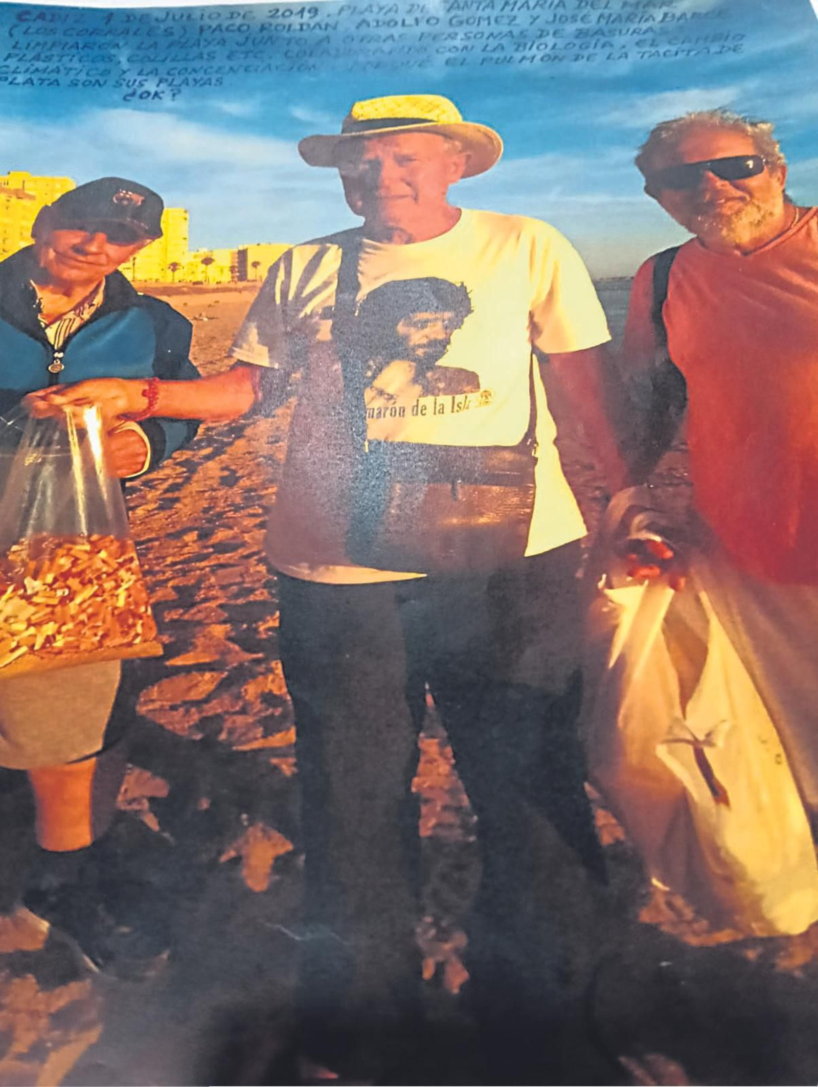 Adolfo Gómez y dos de sus compañeros con una bolsa repleta de colillas recogidas en la playa de Santa María.