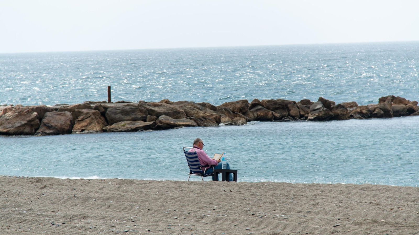 Una personas lee sentado en la playa de Torrenueva Costa.