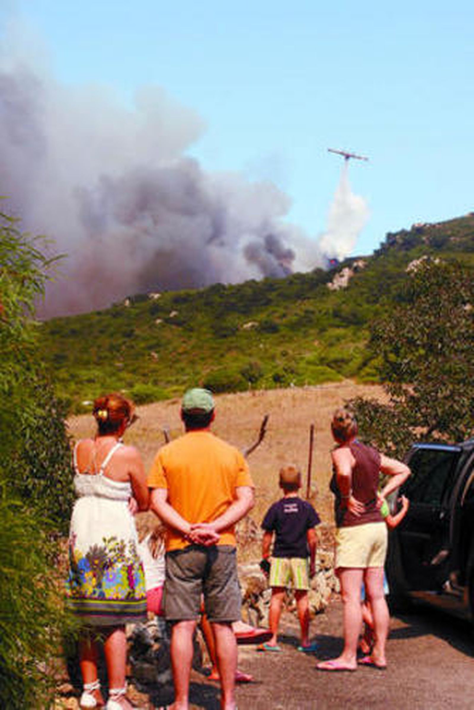 Vecinos de la zona observan las tareas de extinción de los aviones, tras dejar su casa.