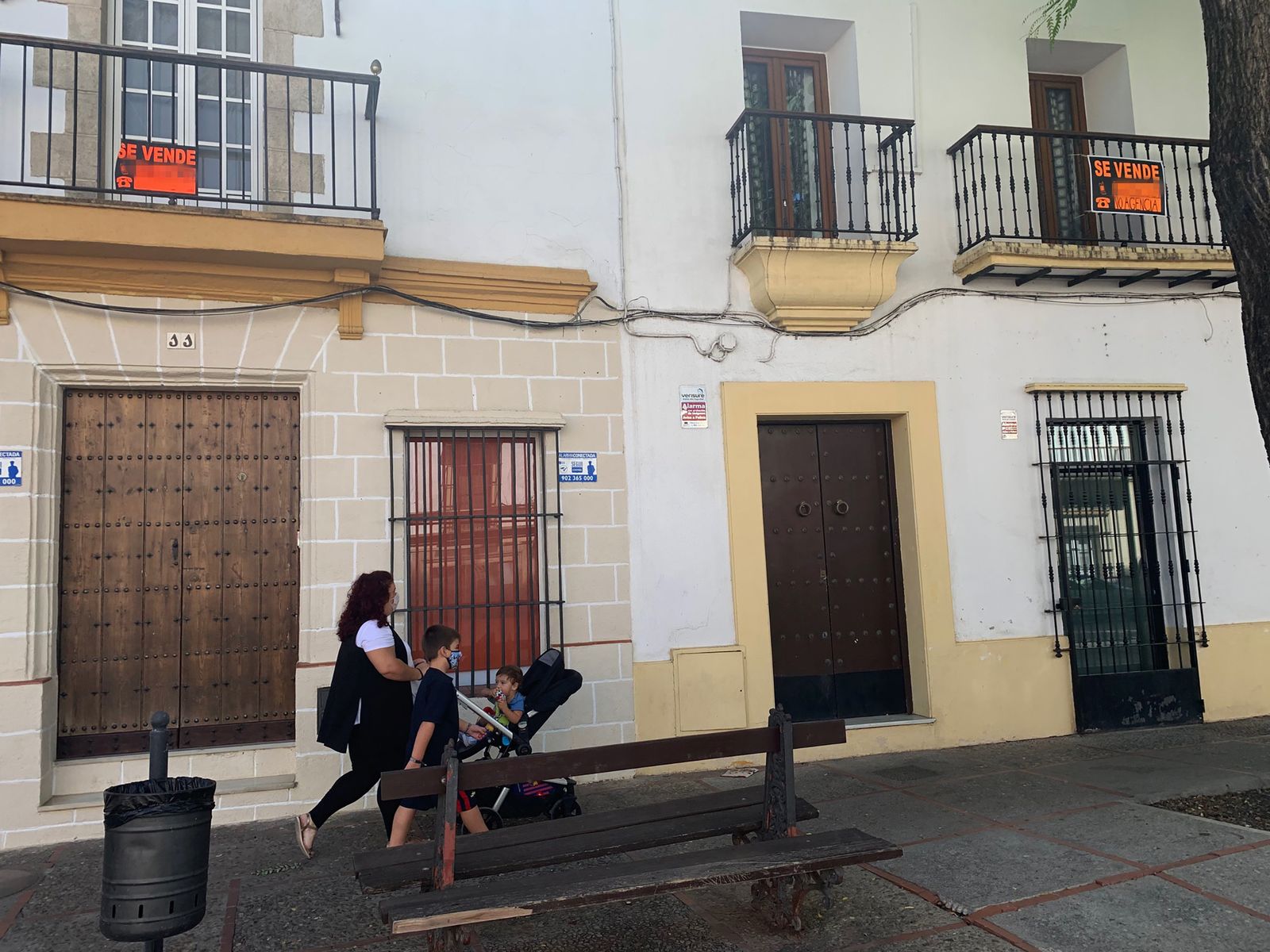 Una mujer pasea en compañía de dos niños junto a dos viviendas a la venta en Jerez.