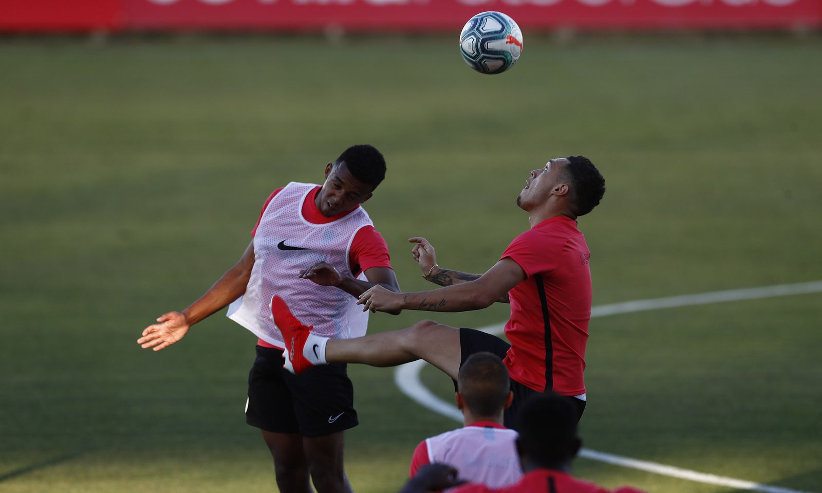 Jules Koundé y Lucas Ocampos saltan con fuerza por un balón alto.