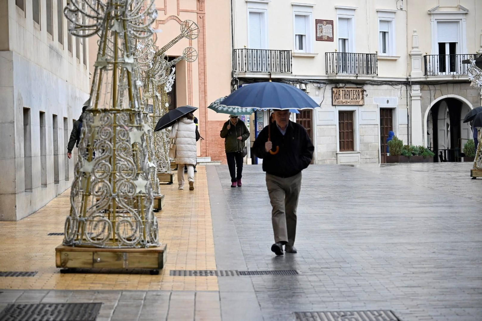 Varias personas se refugian con paraguas de la lluvia en Huelva.