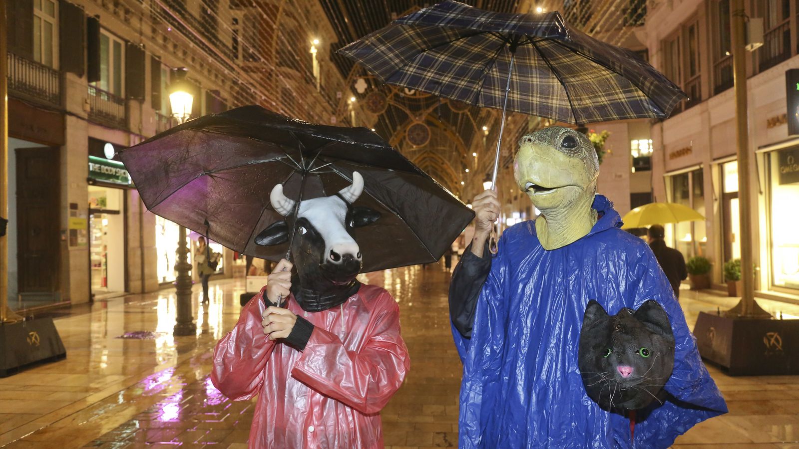 Una pareja con máscaras, chubasquero y paraguas.