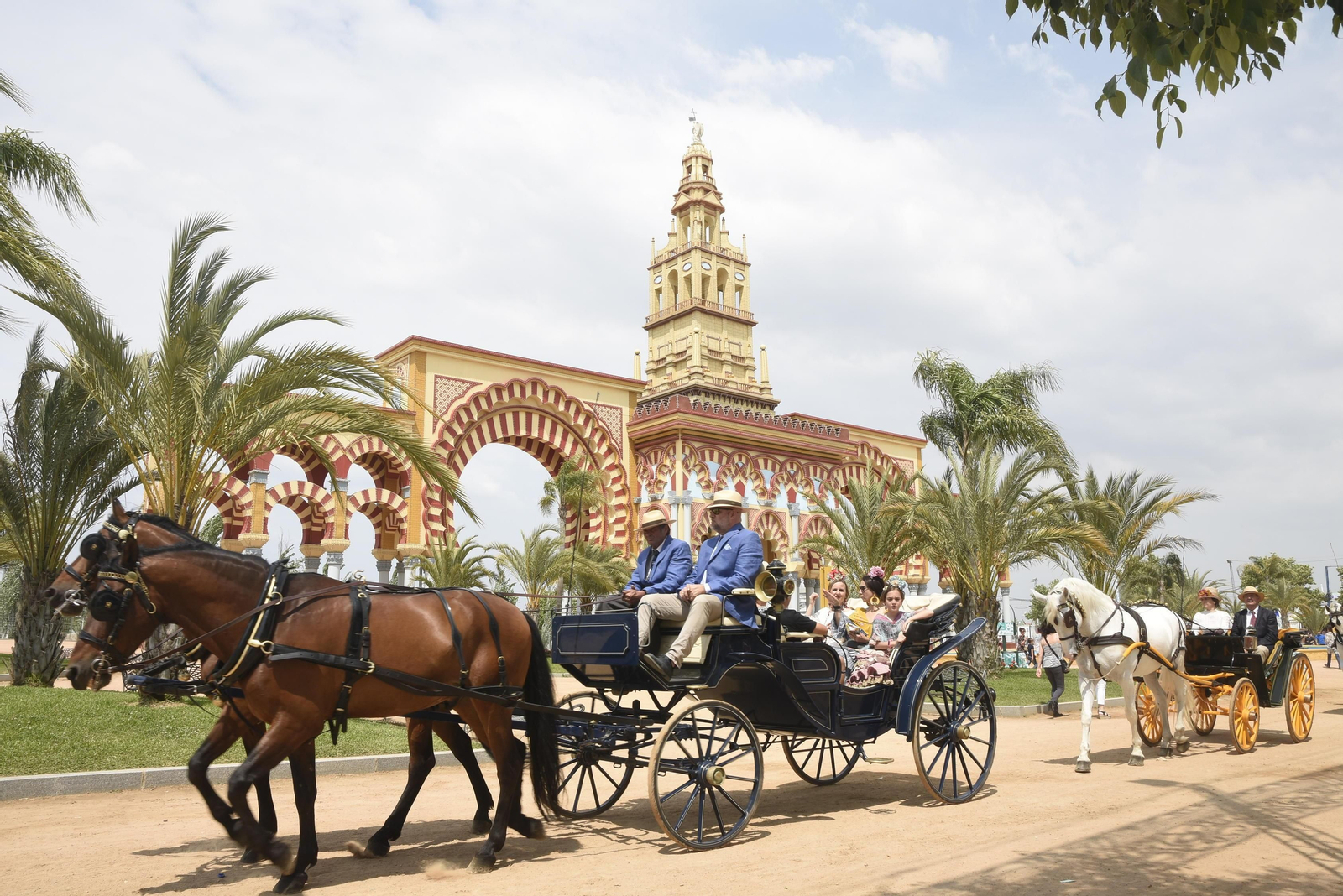 Varios enganches pasean con la portada de la Feria de fondo.