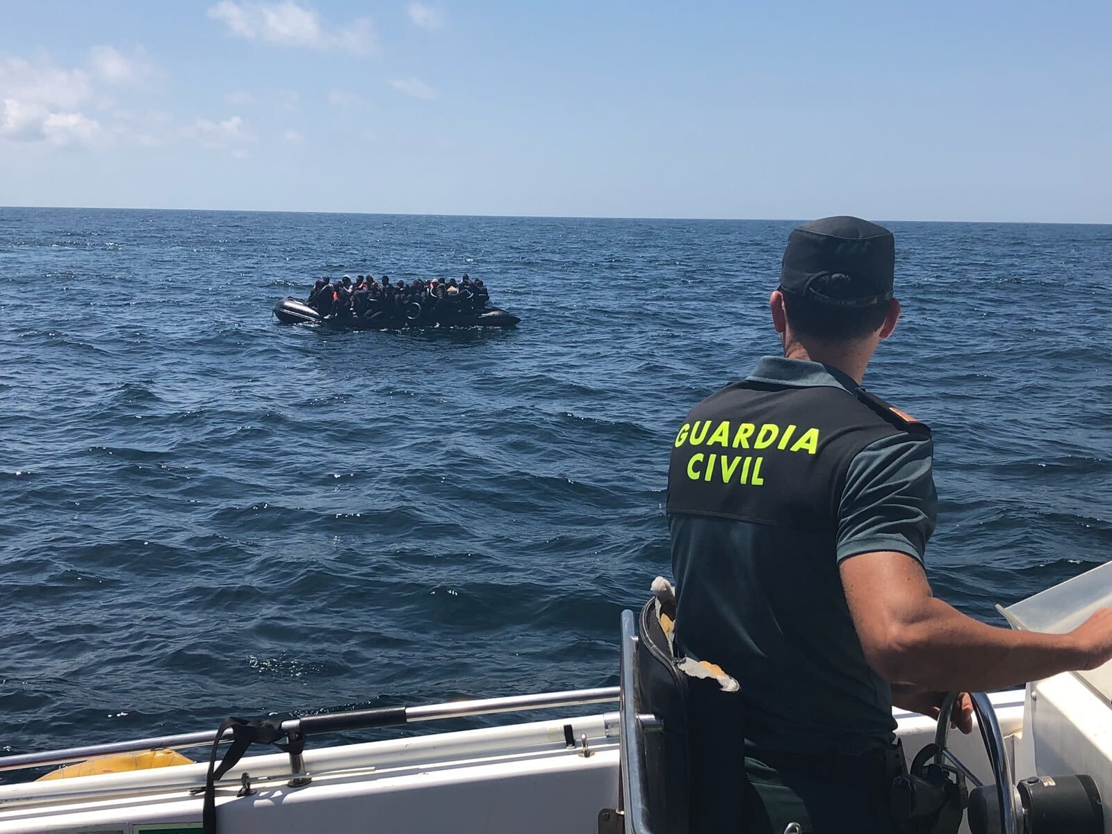 Un Guardia Civil asiste una neumática con migrantes en aguas del Estrecho.