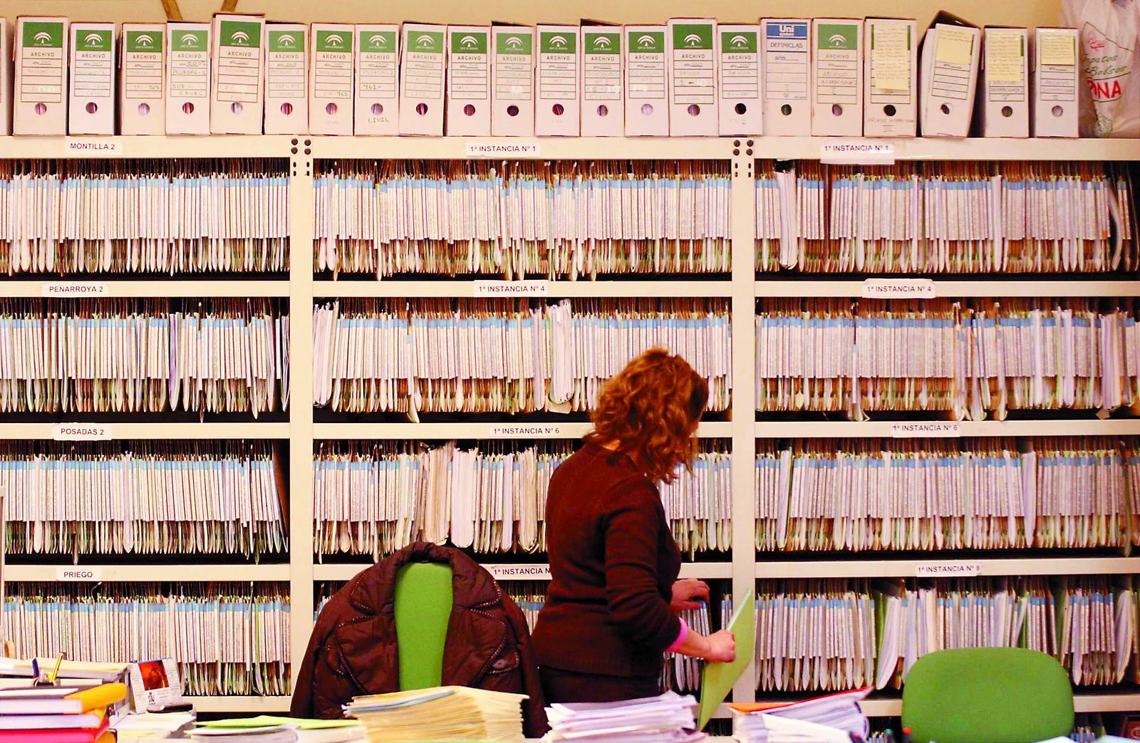 Una funcionaria de Justicia ante una estantería repleta de expedientes.
