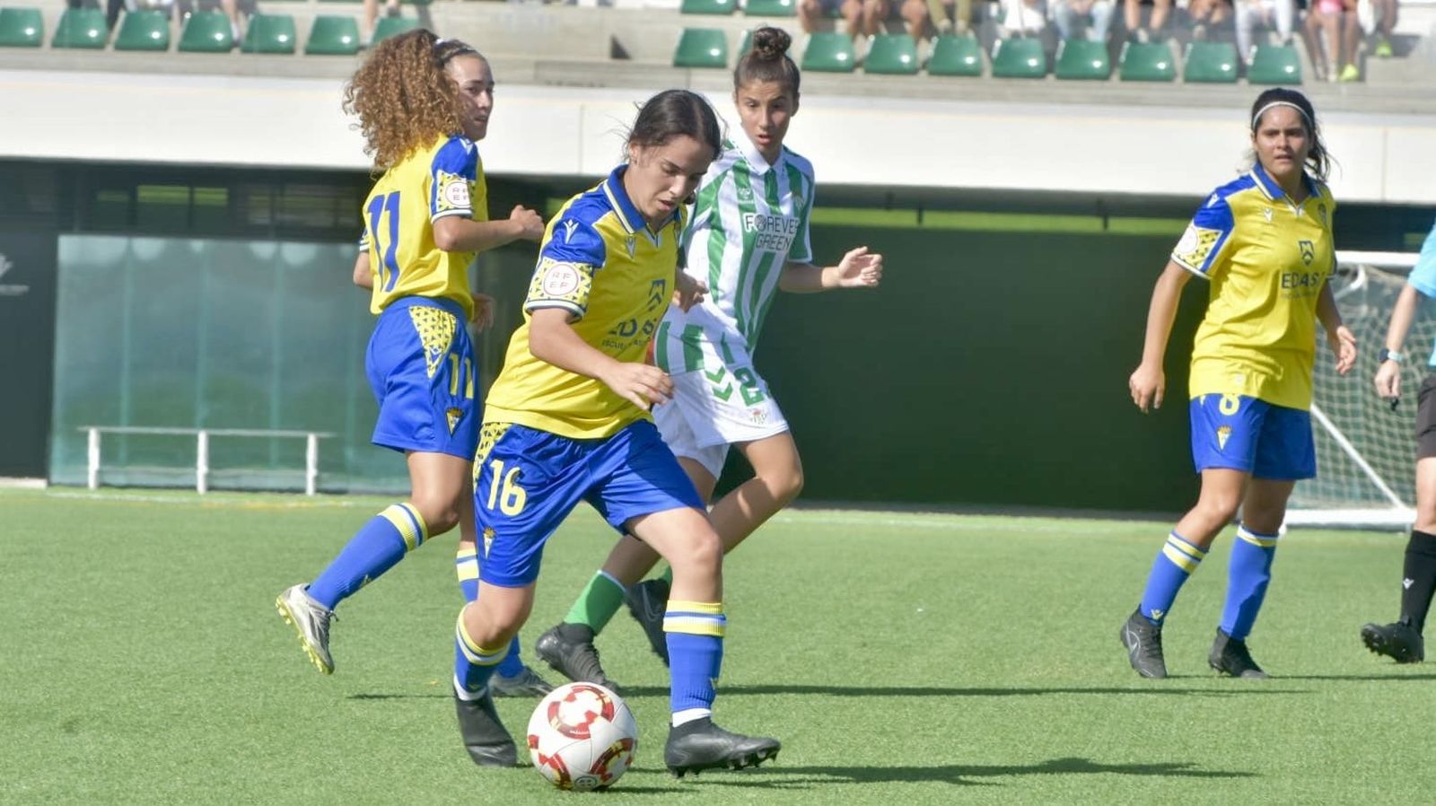 Popi avanza con el balón ante la mirada de sus compañeras María y Lucía.