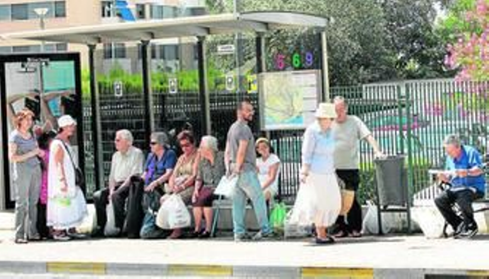 Transeúntes intentan protegerse del sol estival en una marquesina de Emtusa.