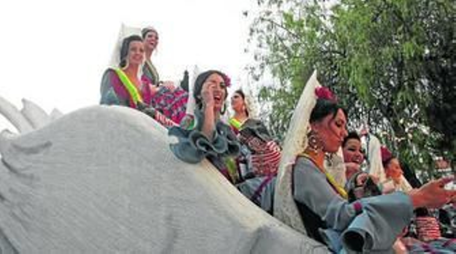 La corte juvenil de la Feria de Los Barrios saluda y lanza caramelos desde su carroza, con formas de cisne.