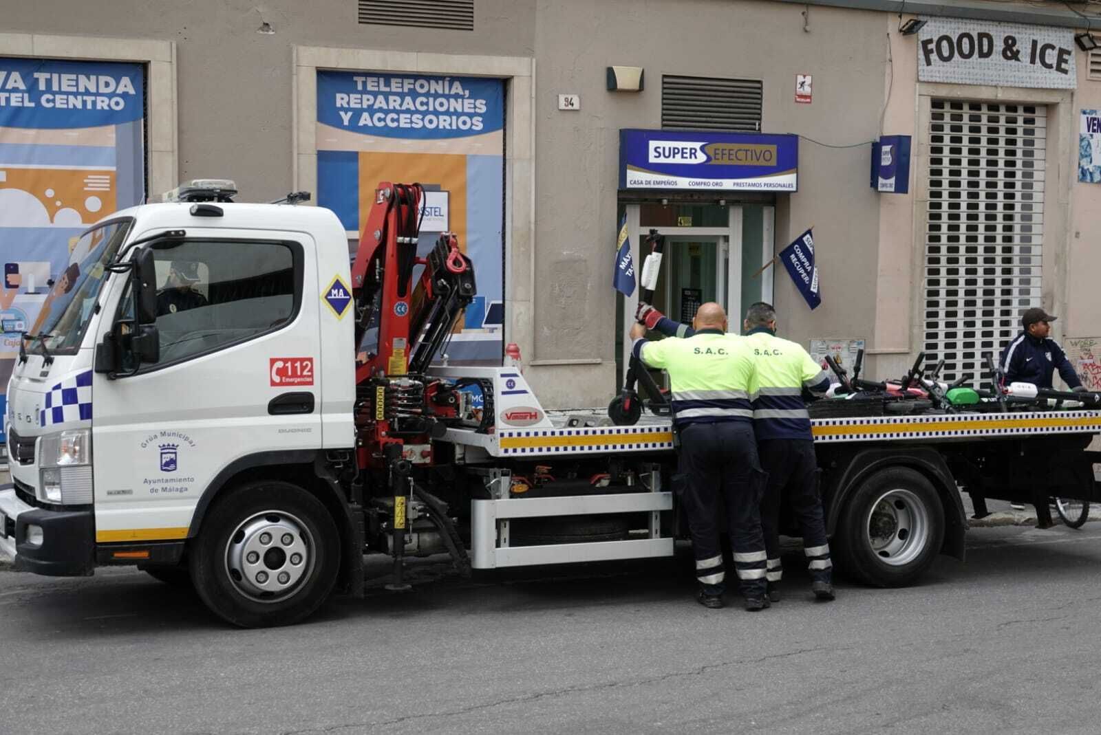 Imagen de dos operarios de la grúa municipal retirando los primeros patinetes eléctricos.