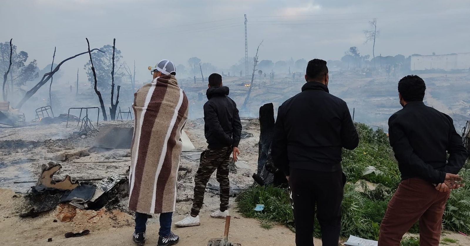 Varias personas observan los efectos del último incendio en el asentamiento de Palos.