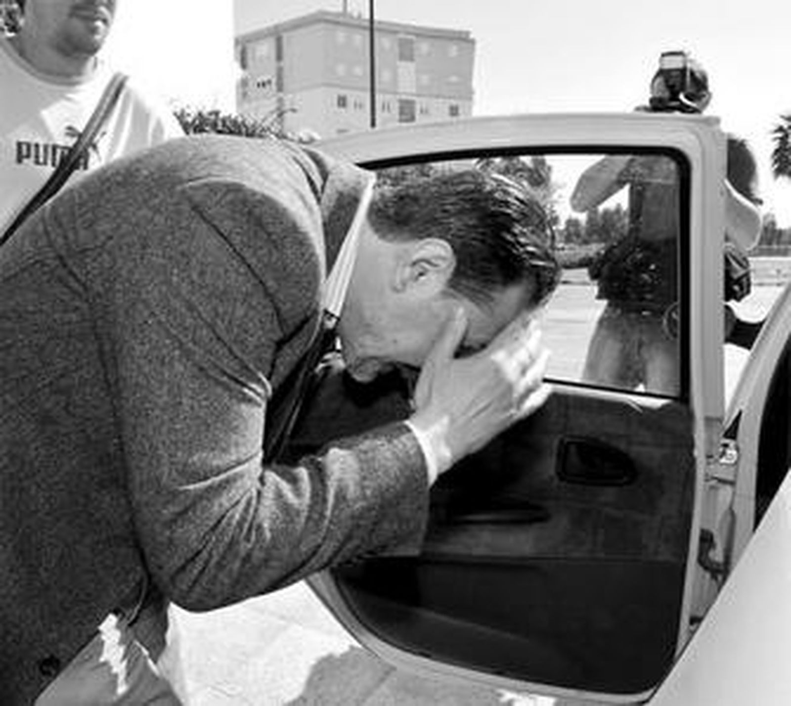 El acusado, protegiéndose la cara poco antes de entrar en el vehículo policial tras el registro.