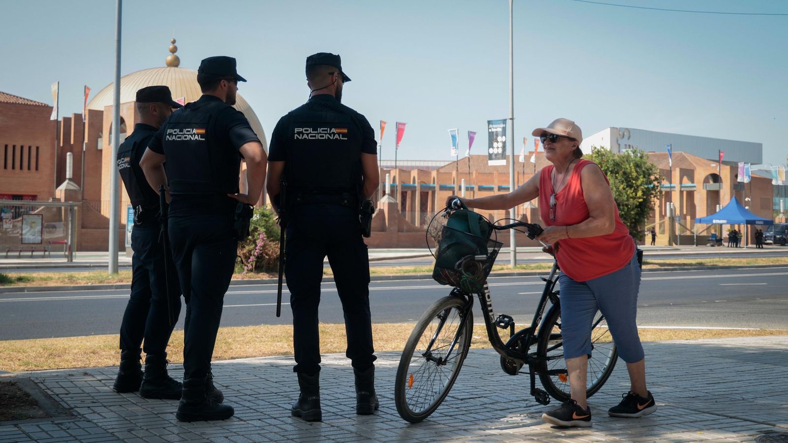 Una mujer pasa empujando su bicicleta ante tres policías, frente a Fibes.