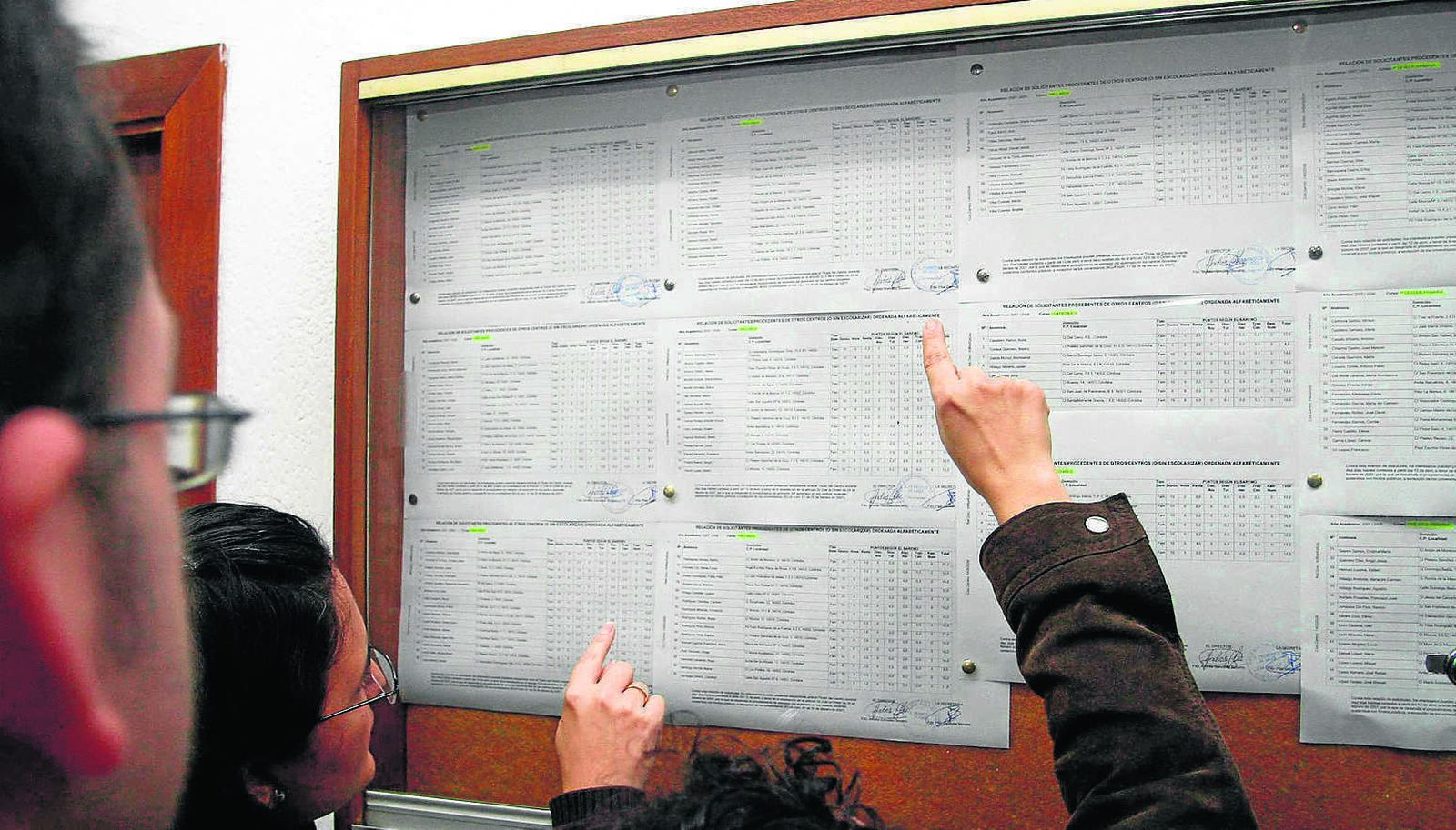 Varias familias comprueban las listas de admitidos en un colegio.