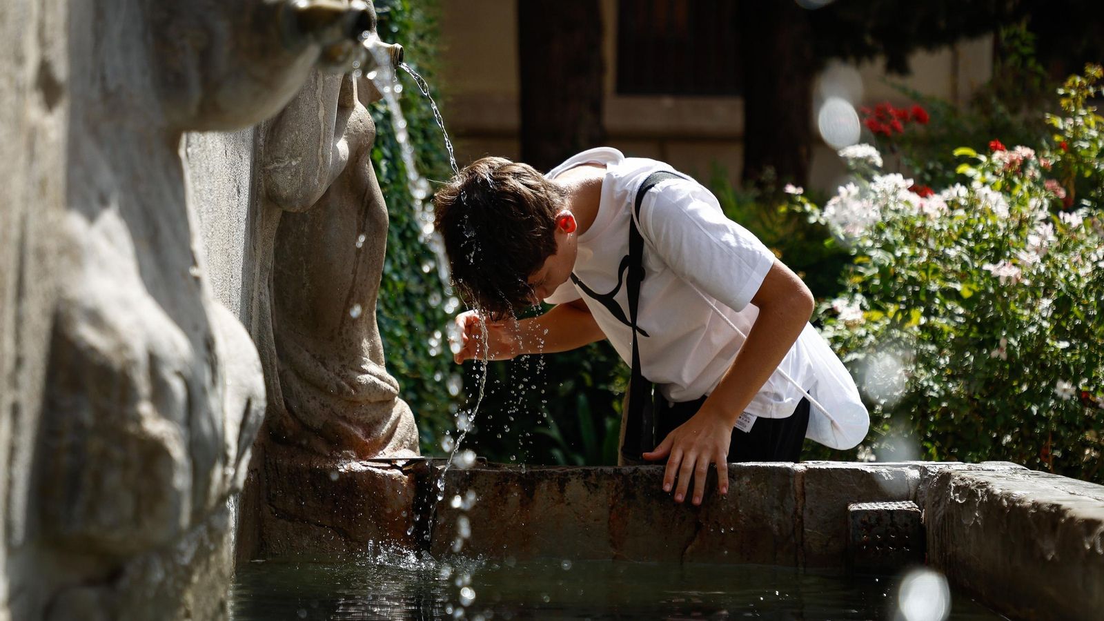Un joven se refresca la cabeza en una fuente durante la primera ola de calor de agosto de 2025 en Granada