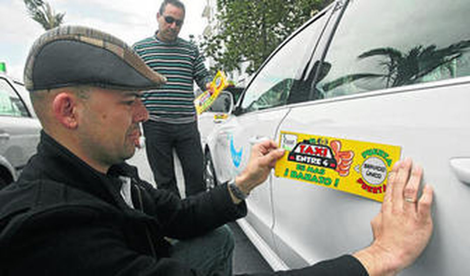 Un taxista pega en su vehículo un adhesivo con el lema 'El taxi entre 4 es más ¡barato!'.