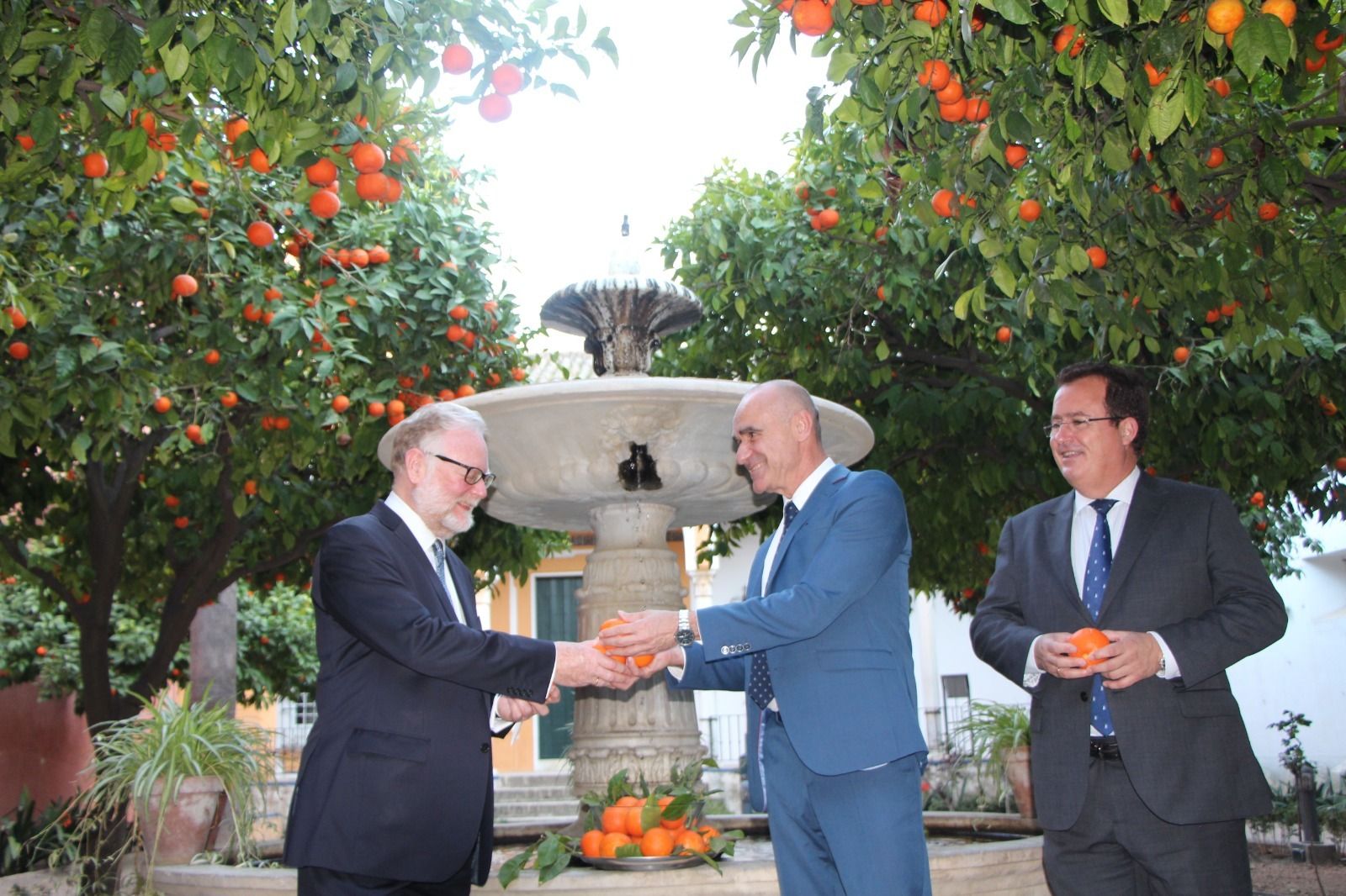 Joe Cooper recoge las naranjas del Alcázar que le ofrece Antonio Muñoz, en presencia de Juan Carlos Cabrera.