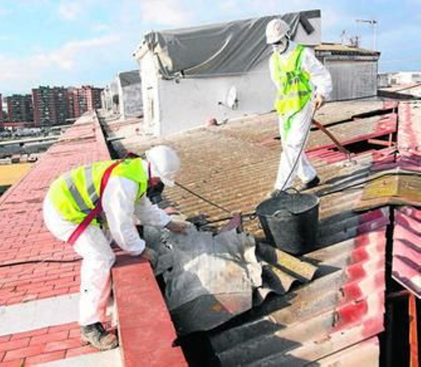 Dos trabajadores retiran planchas de amianto del tejado de un edificio.