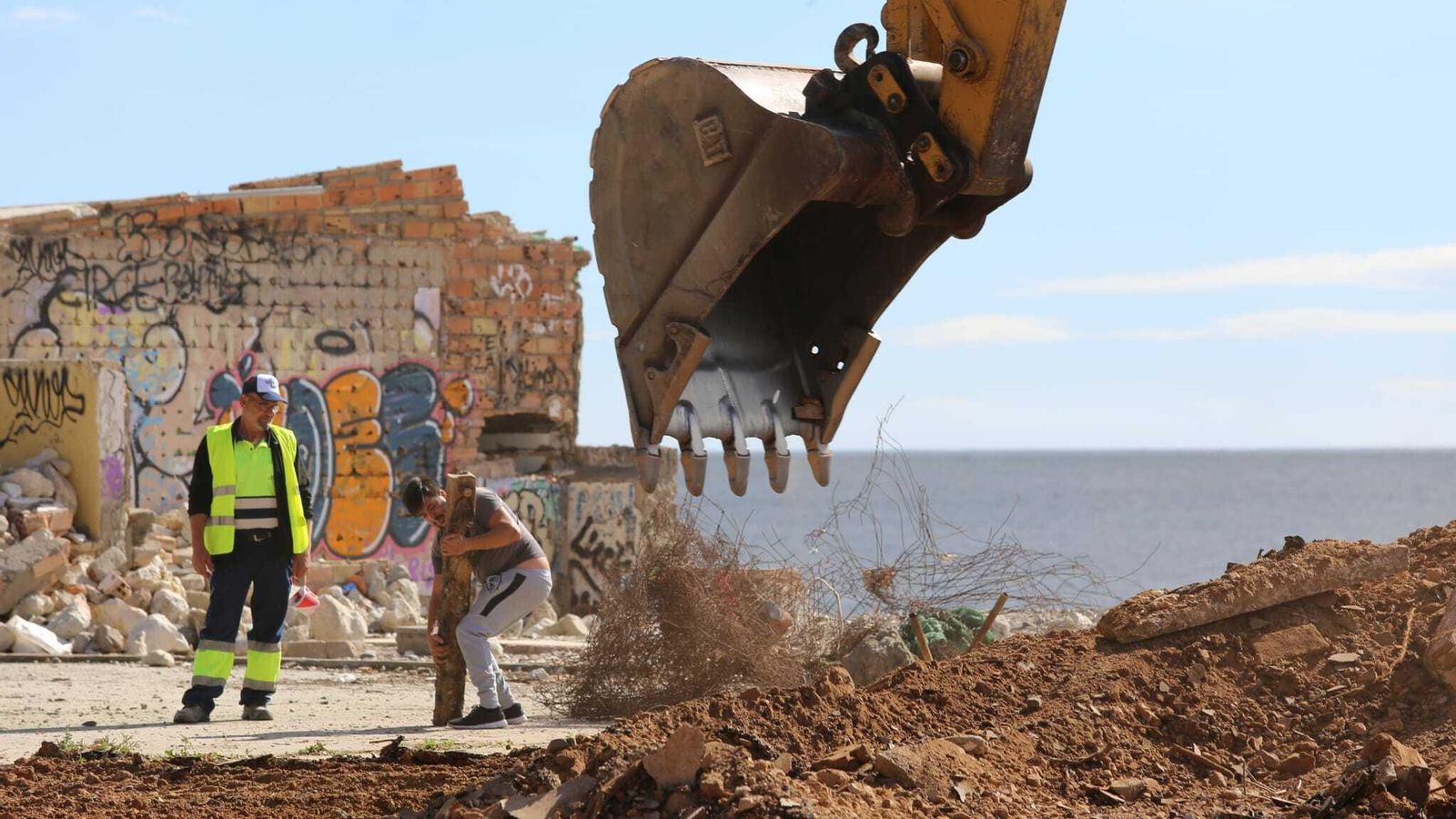 Dos operarios, junto a la máquina encargada de la demolición.