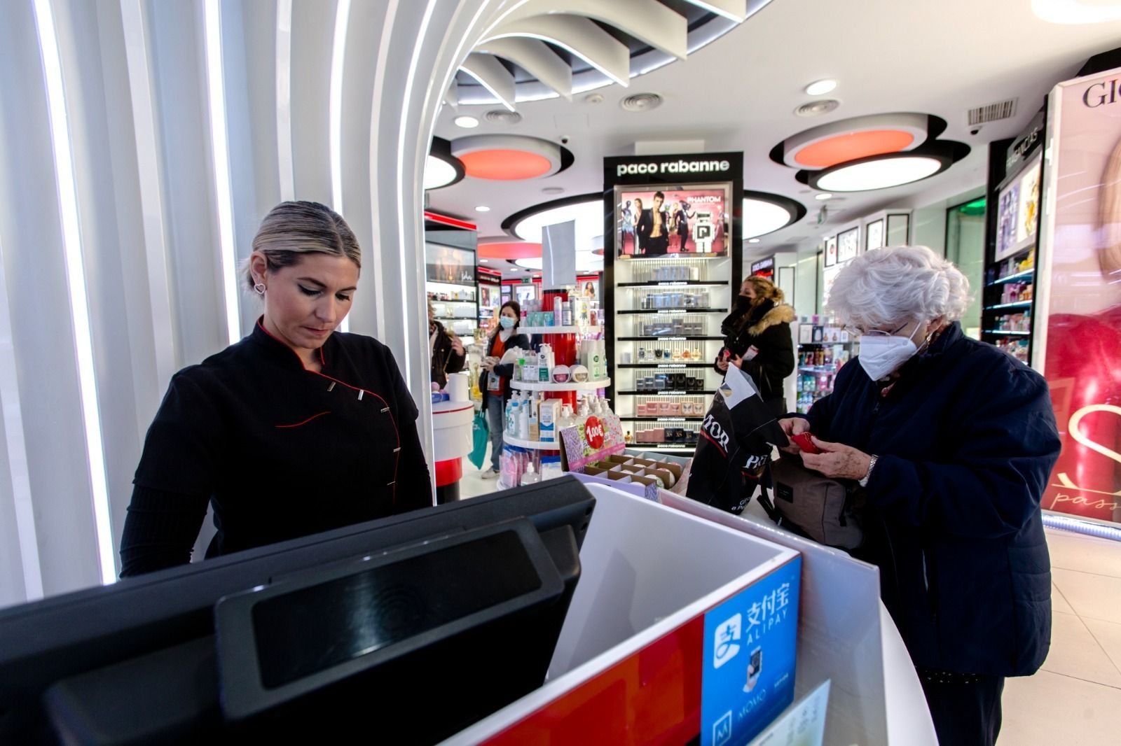 Una dependienta de una perfumería atiende a una clienta que lleva mascarilla.