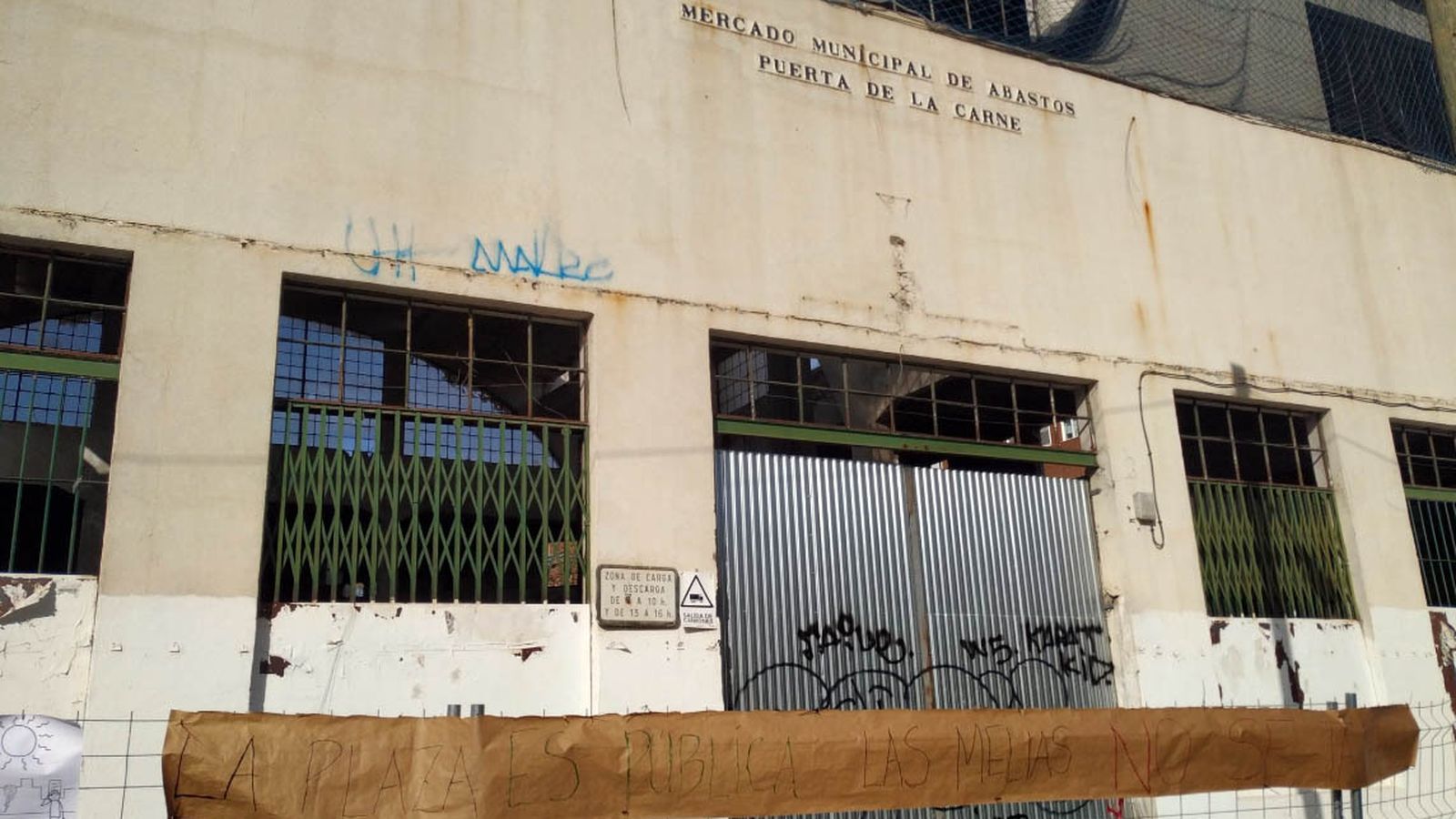 Un cartel con el lema "la plaza es pública y las melias no se talan" en la fachada principal del antiguo mercado.