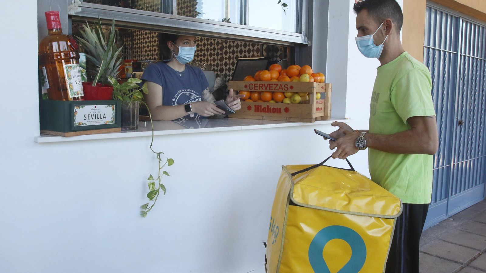 Una camarera entrega un pedido a un repartidor de Glovo en Córdoba.