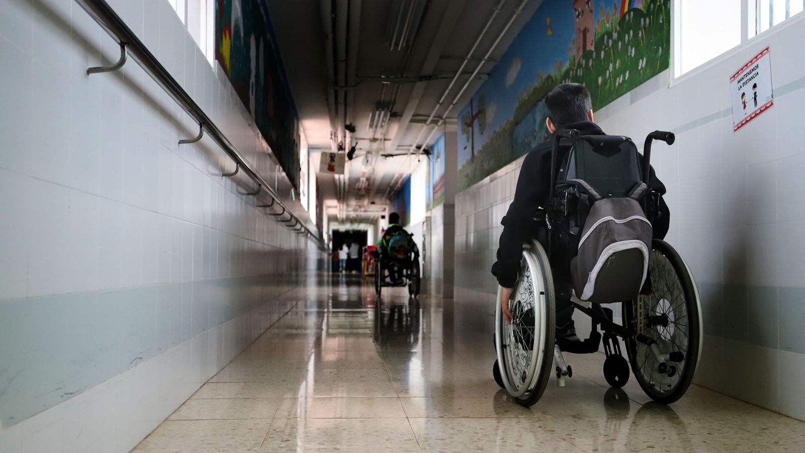 Un joven minusválido se desplaza en silla de ruedas por el pasillo de un centro educativo.