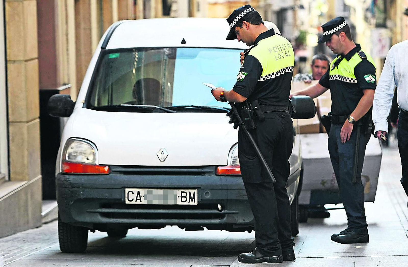 Dos agentes de la Policía Local ponen una multa a un vehículo que se encuentra mal estacionado.