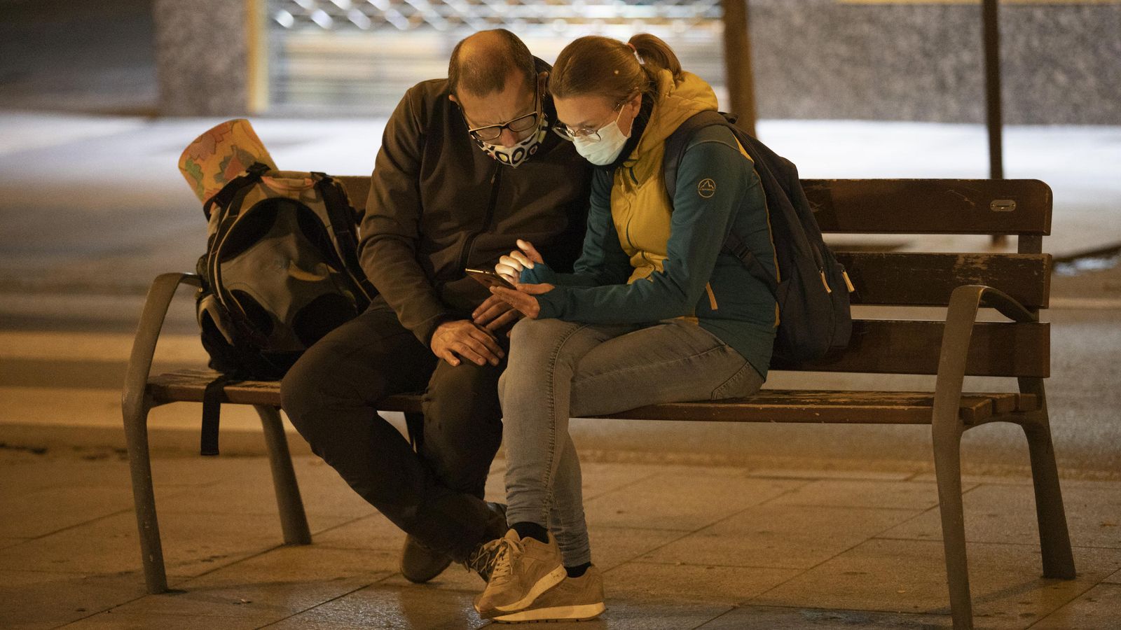 Dos personas miran el móvil sentados en un banco de la capital granadina.