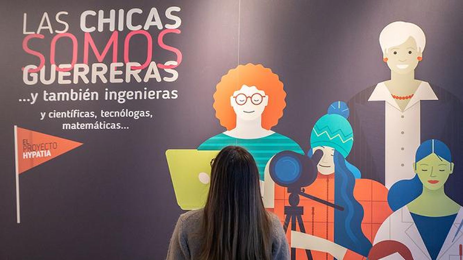 Una joven frente al cartel de la exposición 'Las chicas somos guerreras'