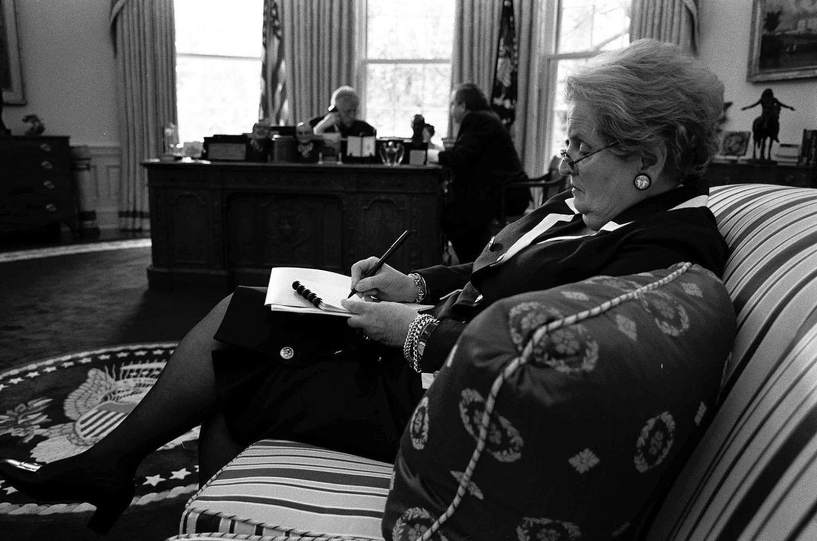 Madeleine Albright toma notas en el Despacho Oval de la Casa Blanca, con Bill Clinton al fondo.