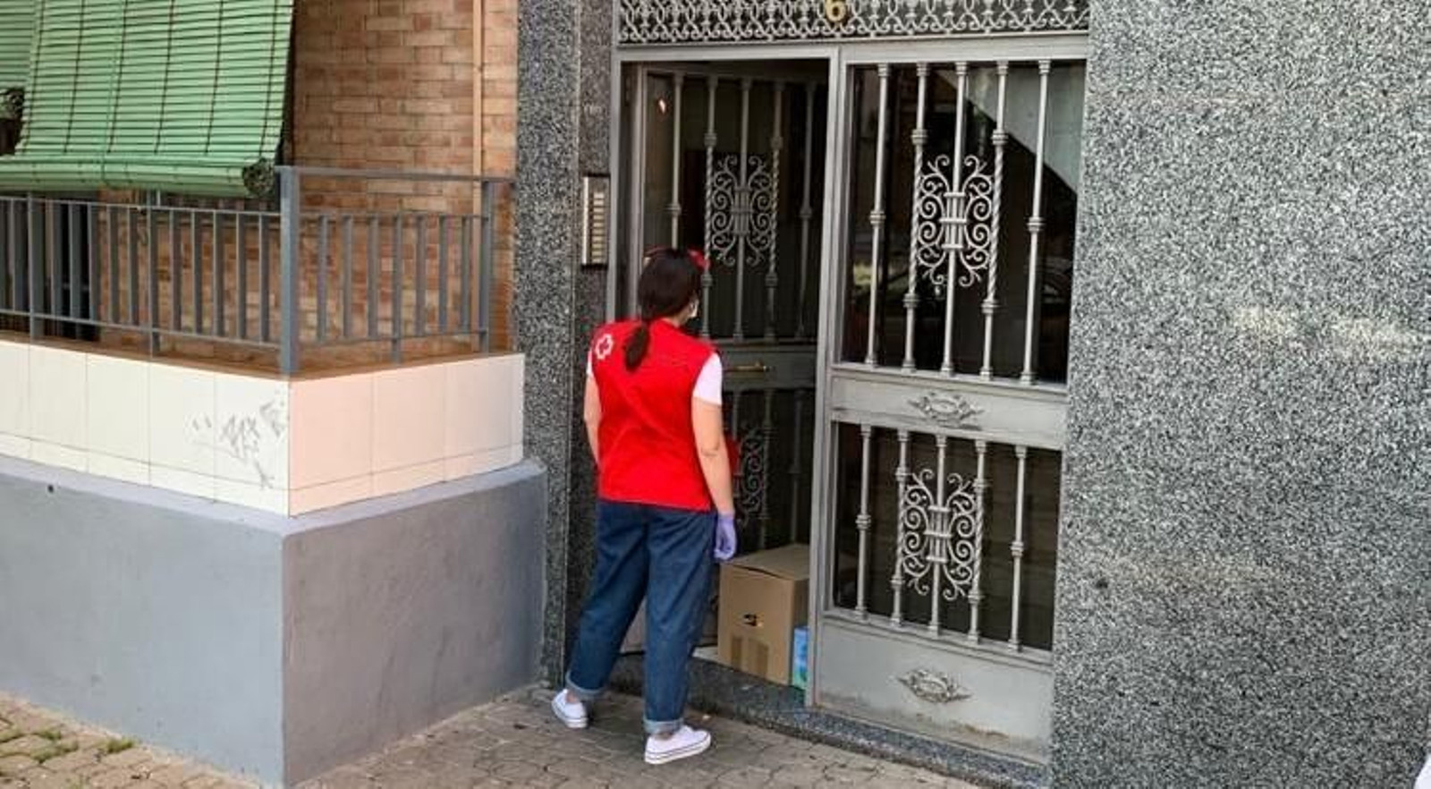 Una voluntaria de Cruz Roja lleva una caja con productos a niños de una familia.