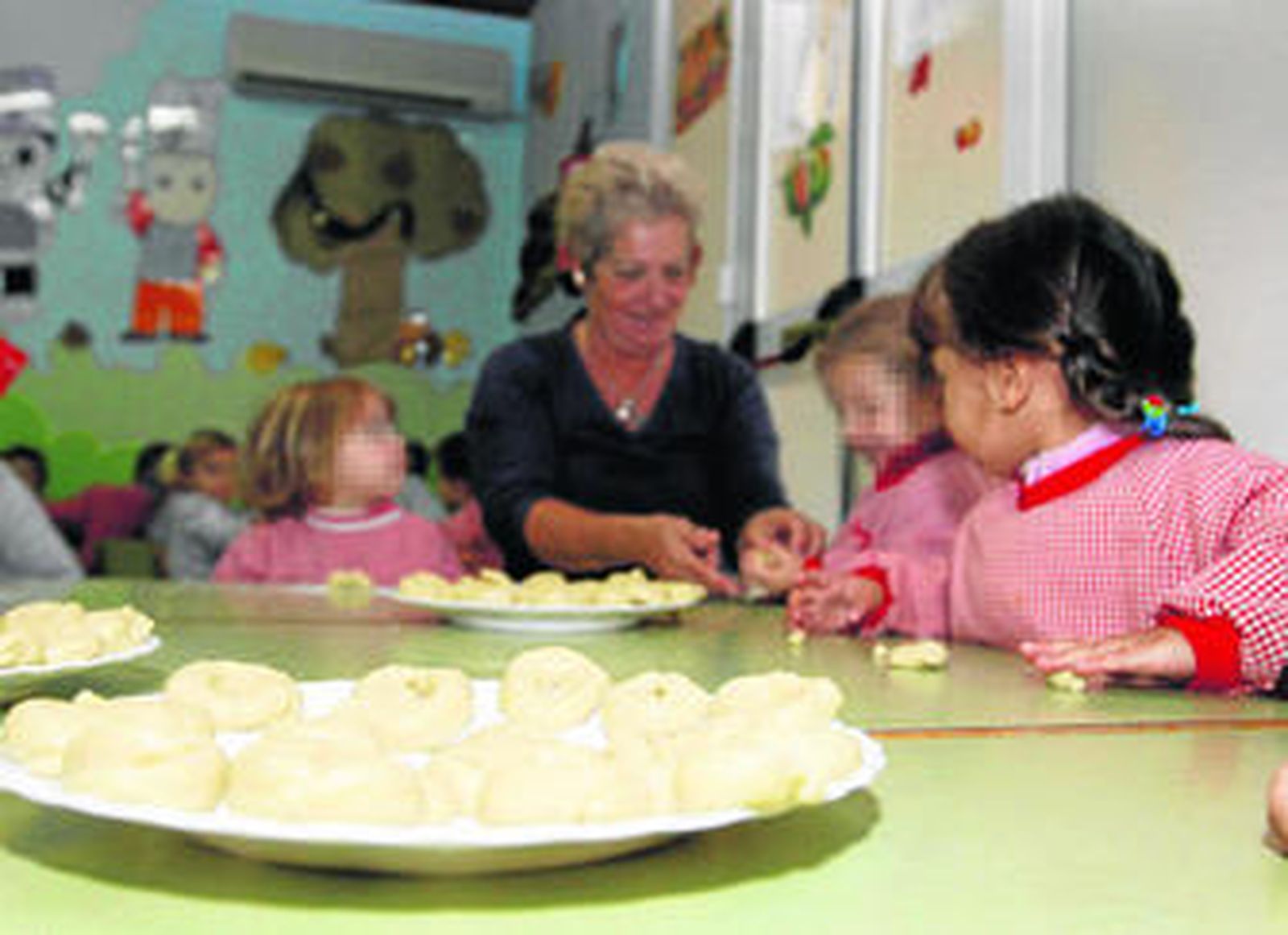 Una abuela enseña a hacer roscos a menores en una guardería.
