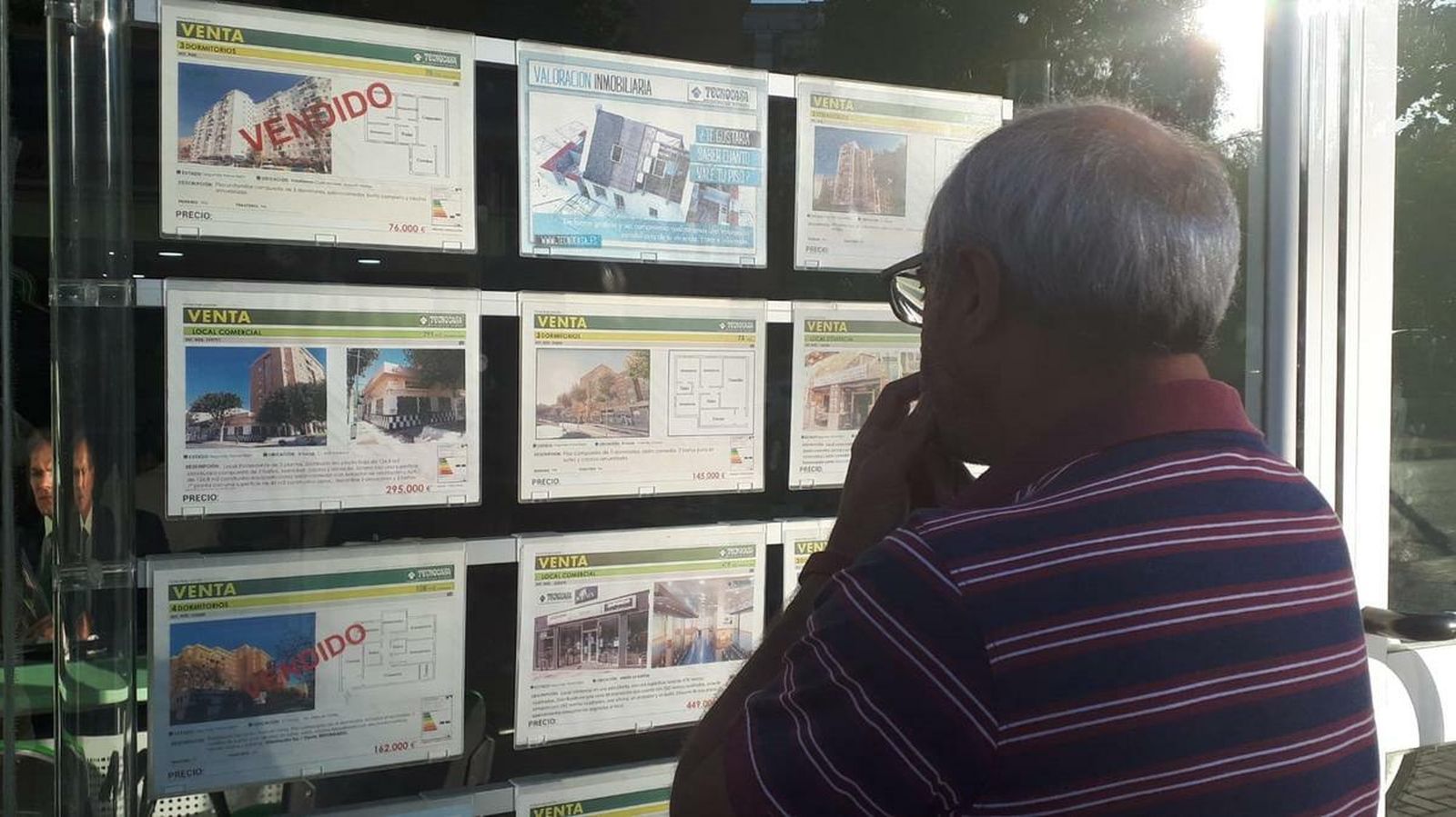 Un hombre mira los anuncios de casas en venta en el escaparate de una inmobiliaria.