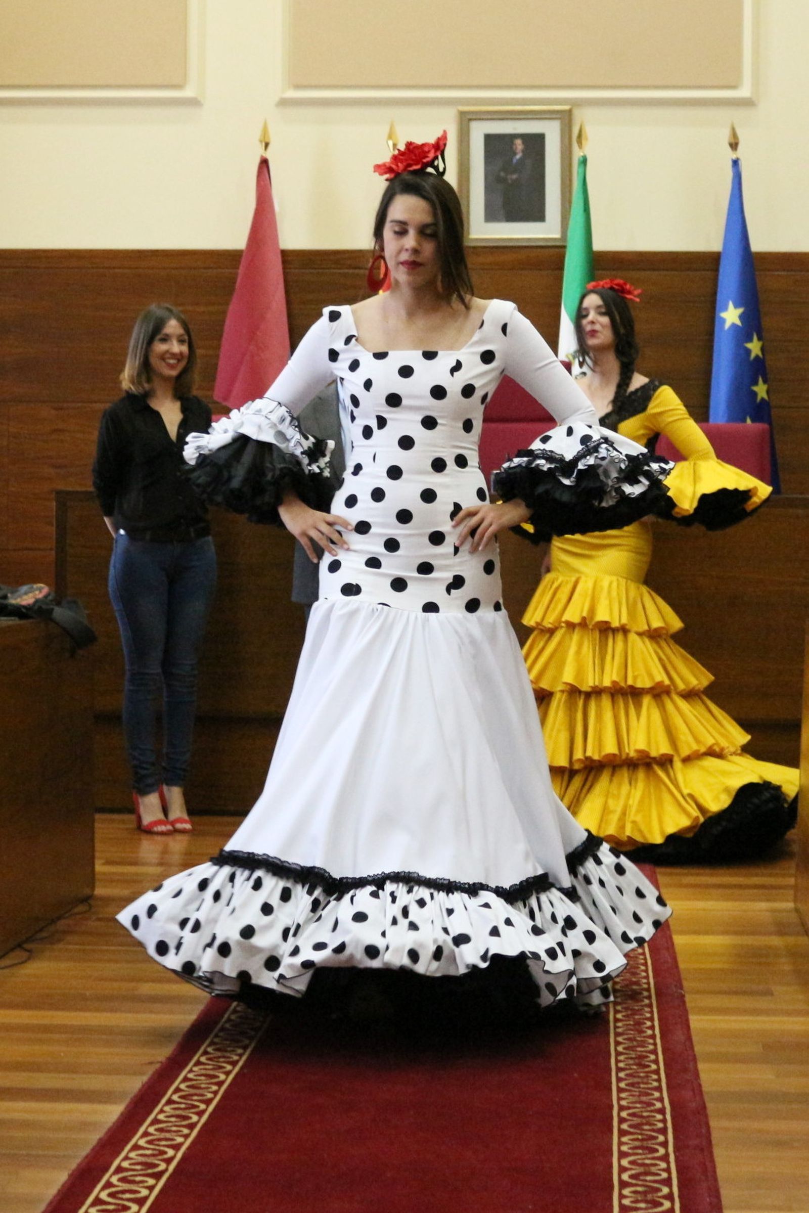 Dos modelos desfilan por el Salón del Plenos del Ayuntamiento ante la mirada de la autora de los trajes.