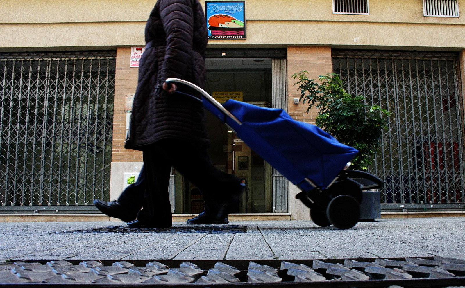 Una mujer acarrea el carrito de la compra frente a un economato de Huelva.