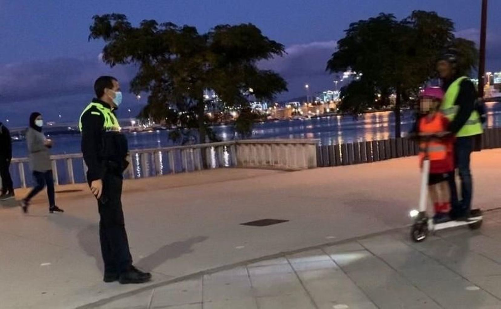 Un policía local se dirige al usuario de un patinete con dos personas