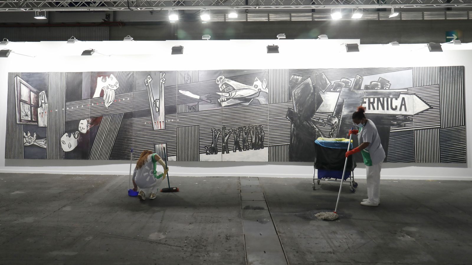 Dos operarias hacen trabajos de limpieza en la sala donde se encuentra la reinterpretación del 'Guernica' de Agustín Ibarrola.