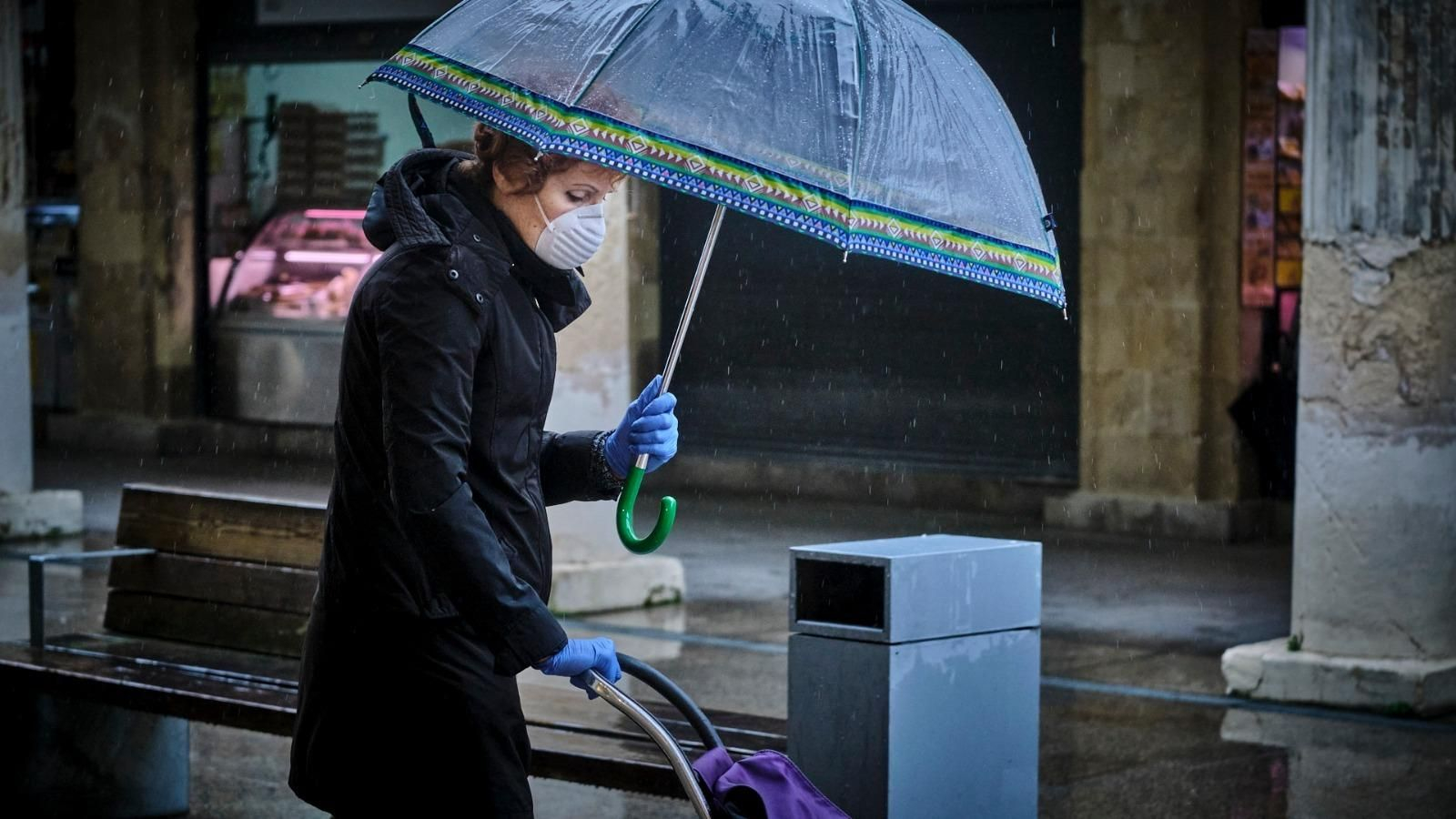 Una señora se protege con la mascarilla en un día de lluvia por el Mercado Central.