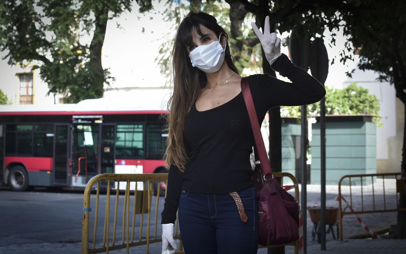 Una joven protegida con mascarilla y guantes hace el signo de la victoria.
