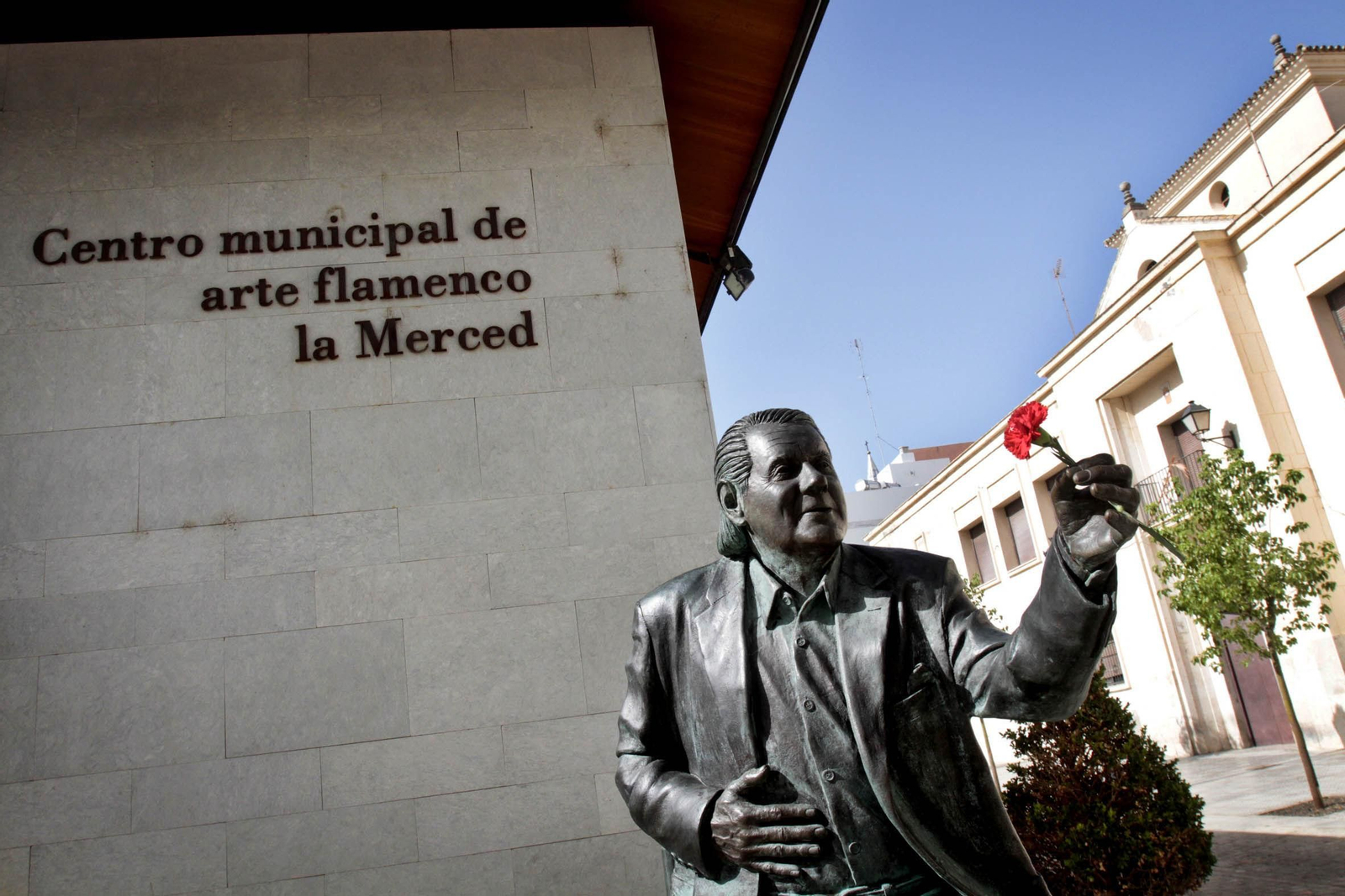 El monumento al cantaor Chano Lobato, frente a la fachada del Centro Municipal de Arte Flamenco  la Merced, con un clavel que fue colocado por un vecino
