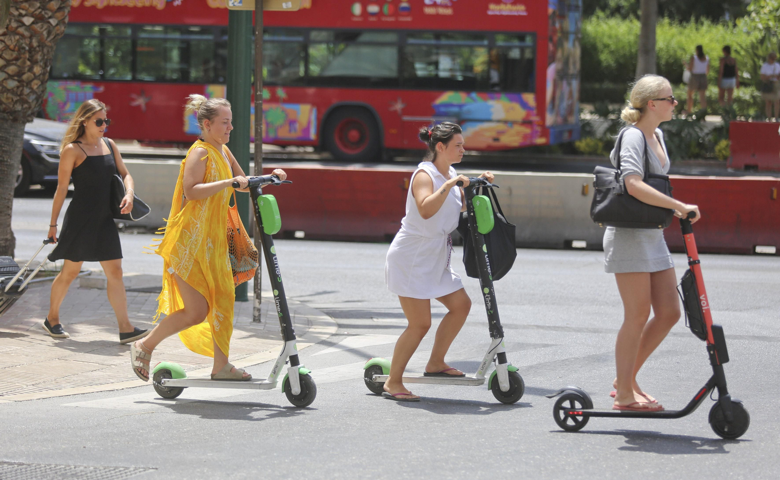 Tres mujeres cruzan un paso de peatones con sus respectivos patinetes de alquiler. Tres mujeres cruzan un paso de peatones con sus respectivos patinetes de alquiler.