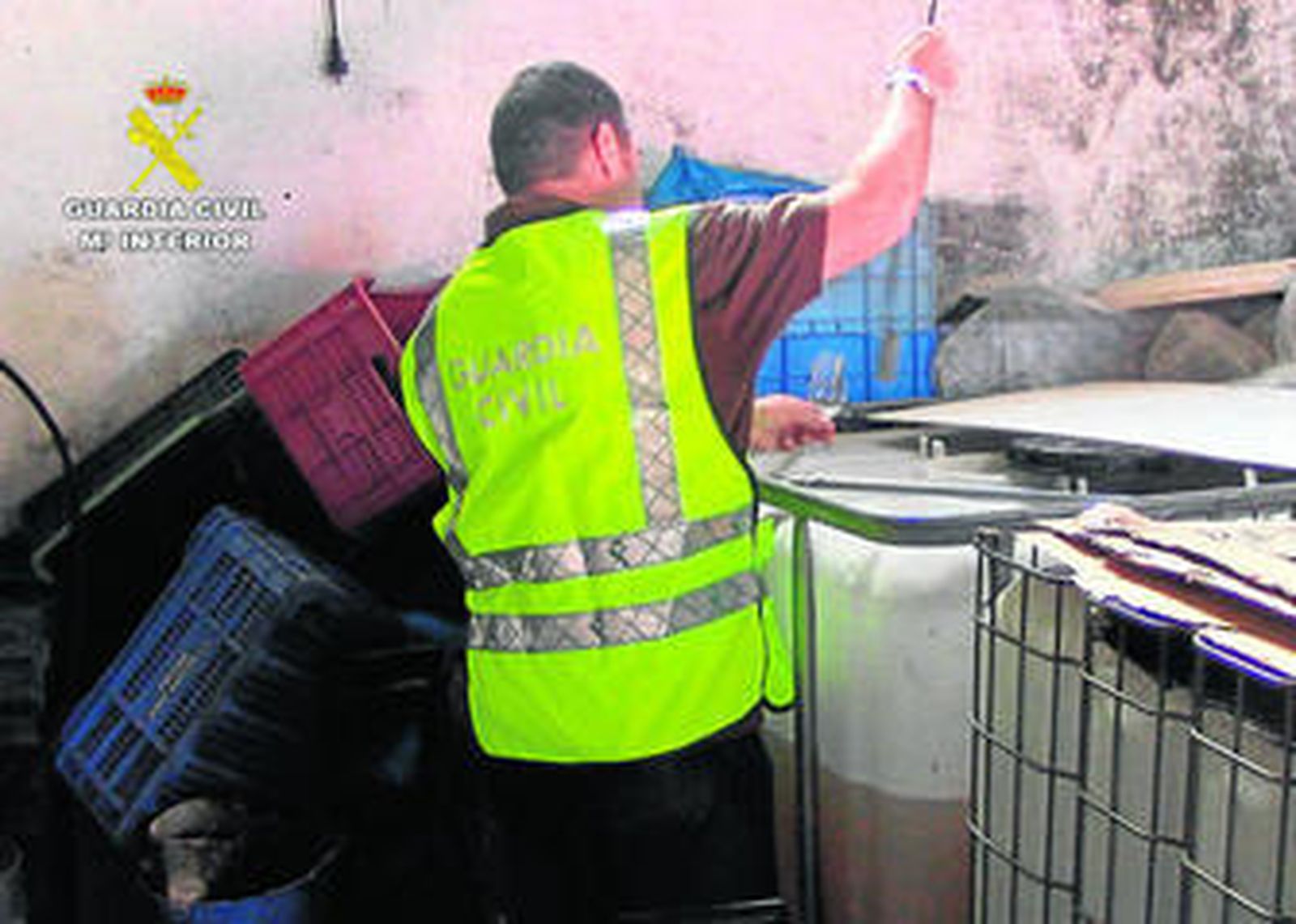 Un agente del Seprona junto a los contenedores de plástico en los que se almacenaba el vino en la bodega clausurada.
