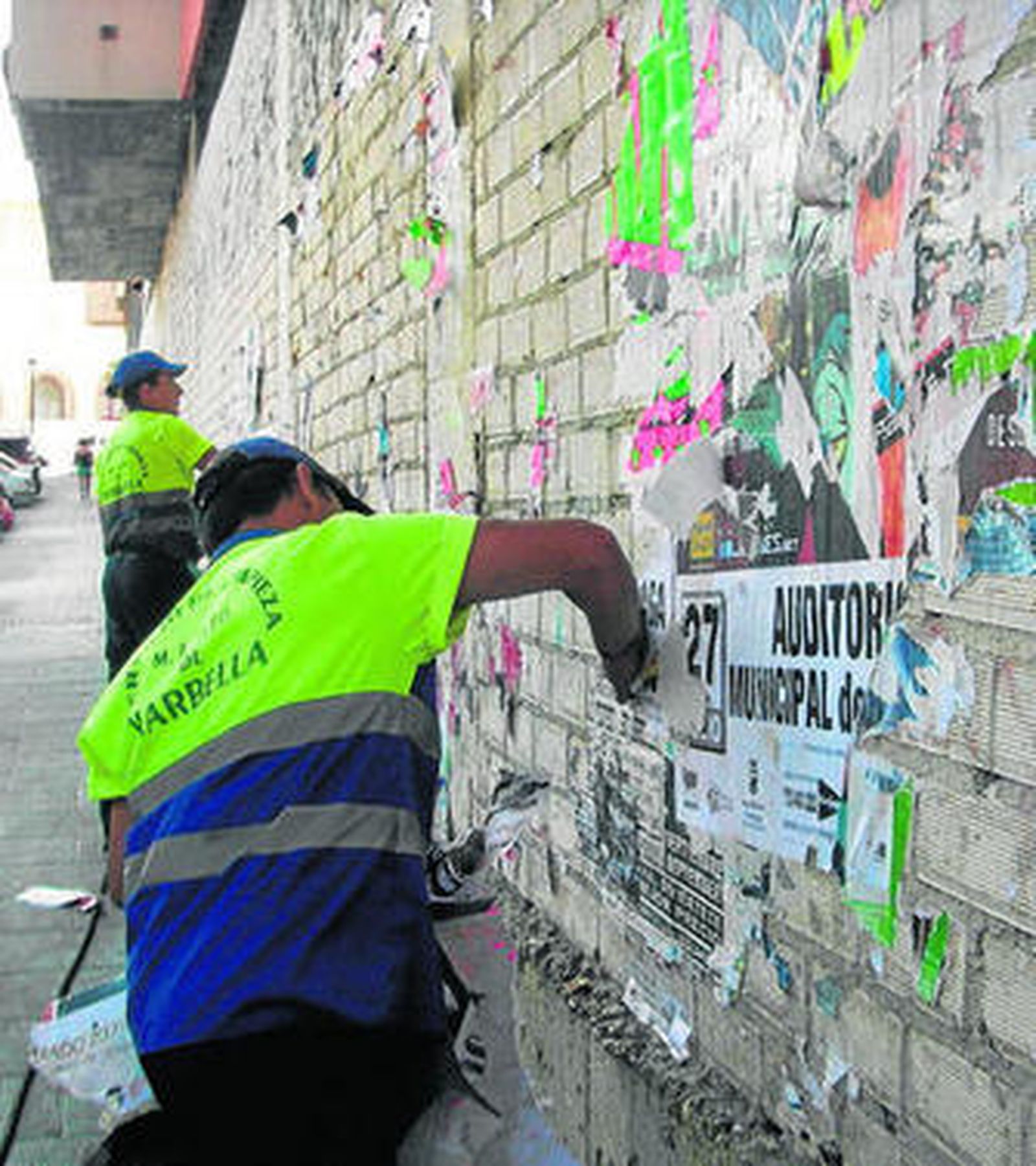 Operarios de limpieza retiran carteles publicitarios de una pared.