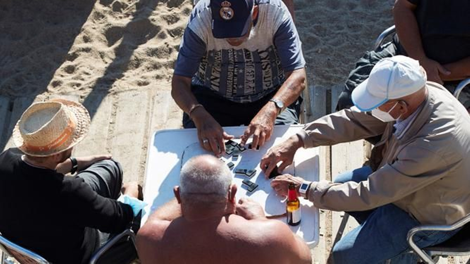 Varias personas juegan al dominó en un bar de la playa de La Barceloneta.