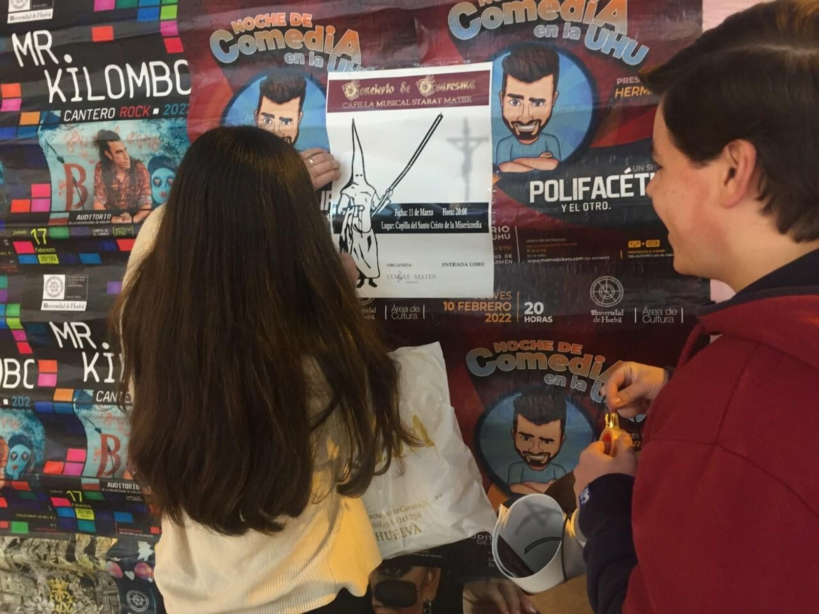 Dos jóvenes pegan un cartel de un acto cofrade en una valla de la calle Concepción.