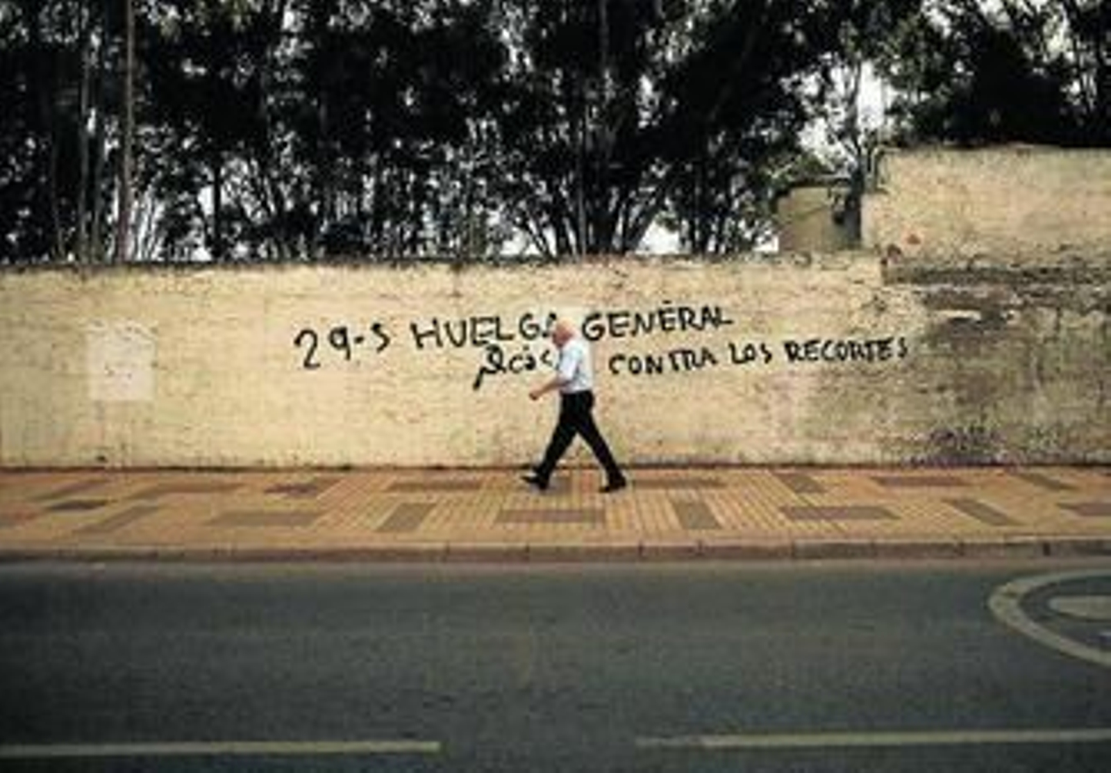 Una persona pasea junto a una pintada sobre la huelga general.