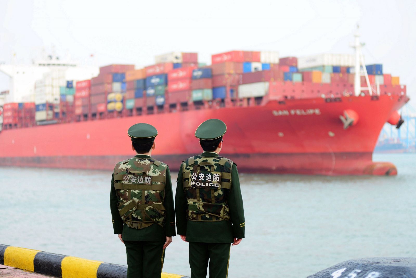 Dos guardias fronterizos ante un barco cargado de contenedores mientras hacen guardia en el puerto chino de Qingdao.
